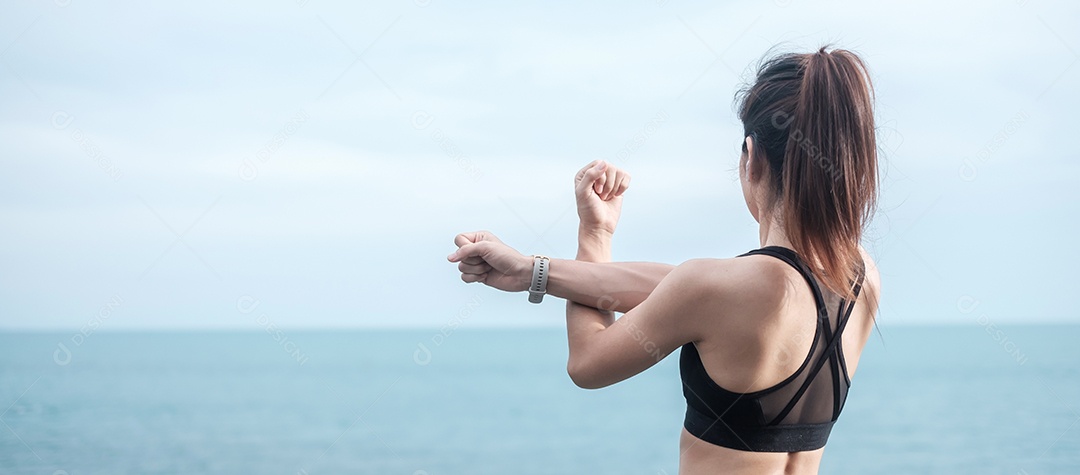 Fêmea jovem fitness em roupas esportivas esticando o corpo contra o oceano.