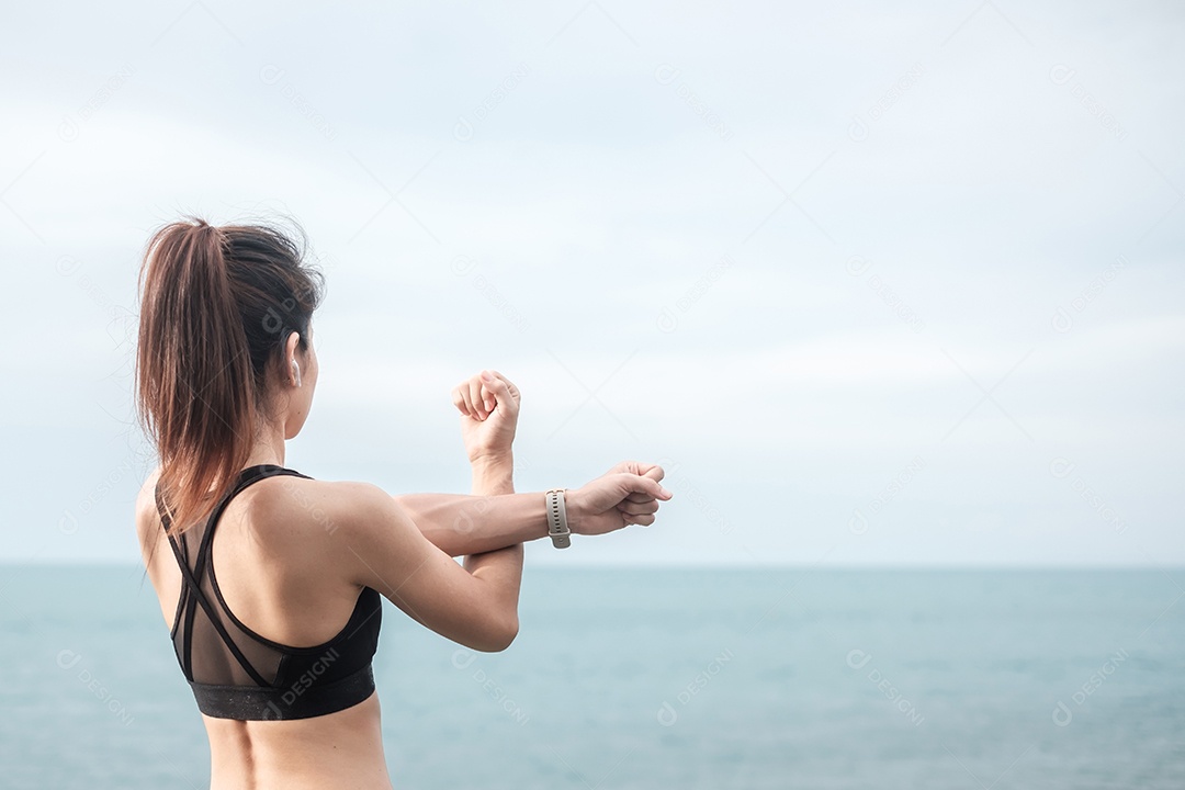 Fêmea jovem fitness em roupas esportivas esticando o corpo contra o oceano.