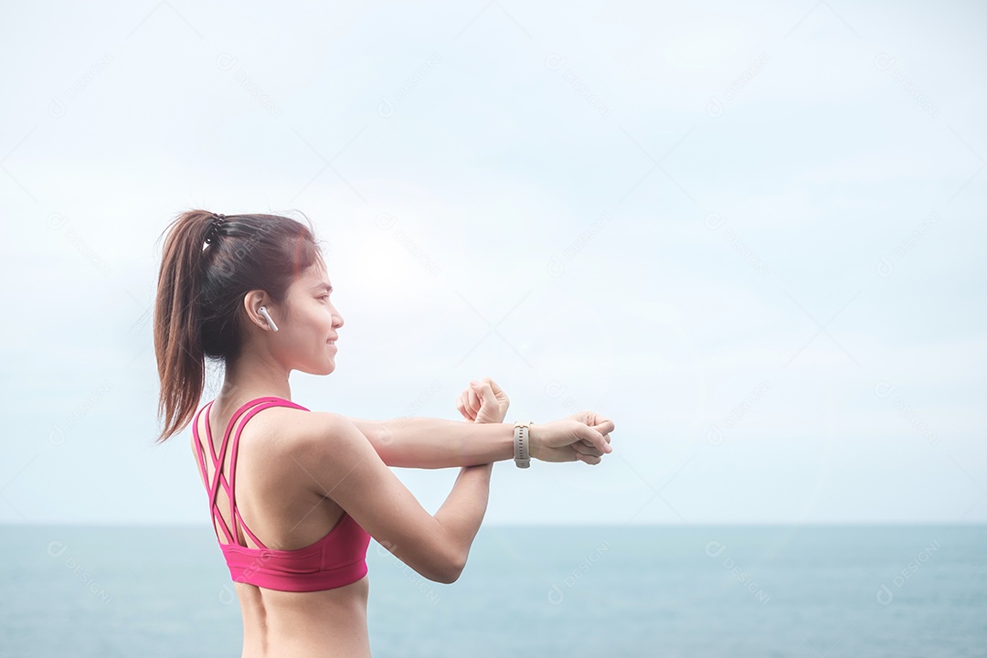 Fêmea jovem fitness em roupas esportivas esticando o corpo contra o oceano.