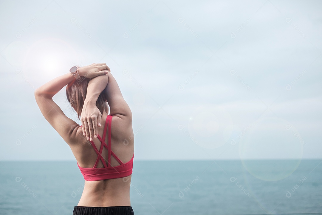 Fêmea jovem fitness em roupas esportivas esticando o corpo contra o oceano.