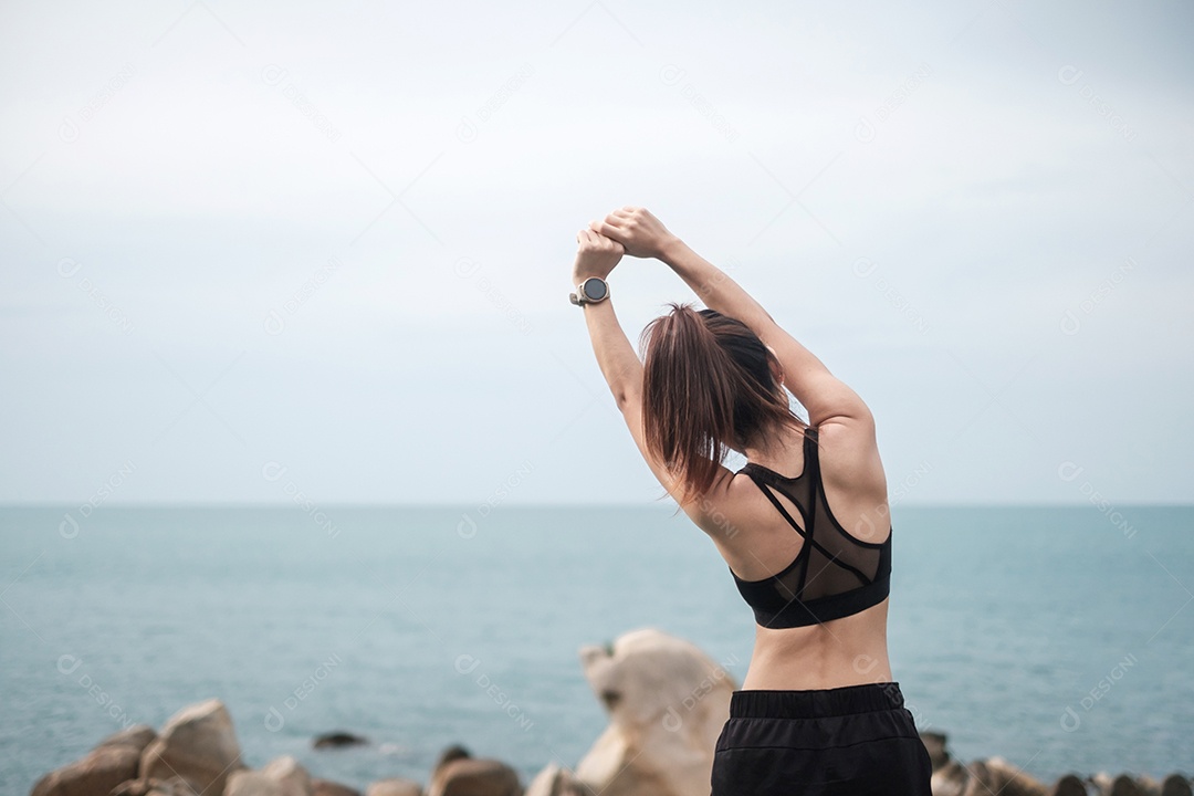 Fêmea jovem fitness em roupas esportivas esticando o corpo contra o oceano.