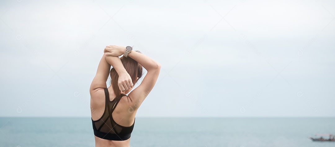 Fêmea jovem fitness em roupas esportivas esticando o corpo contra o oceano.