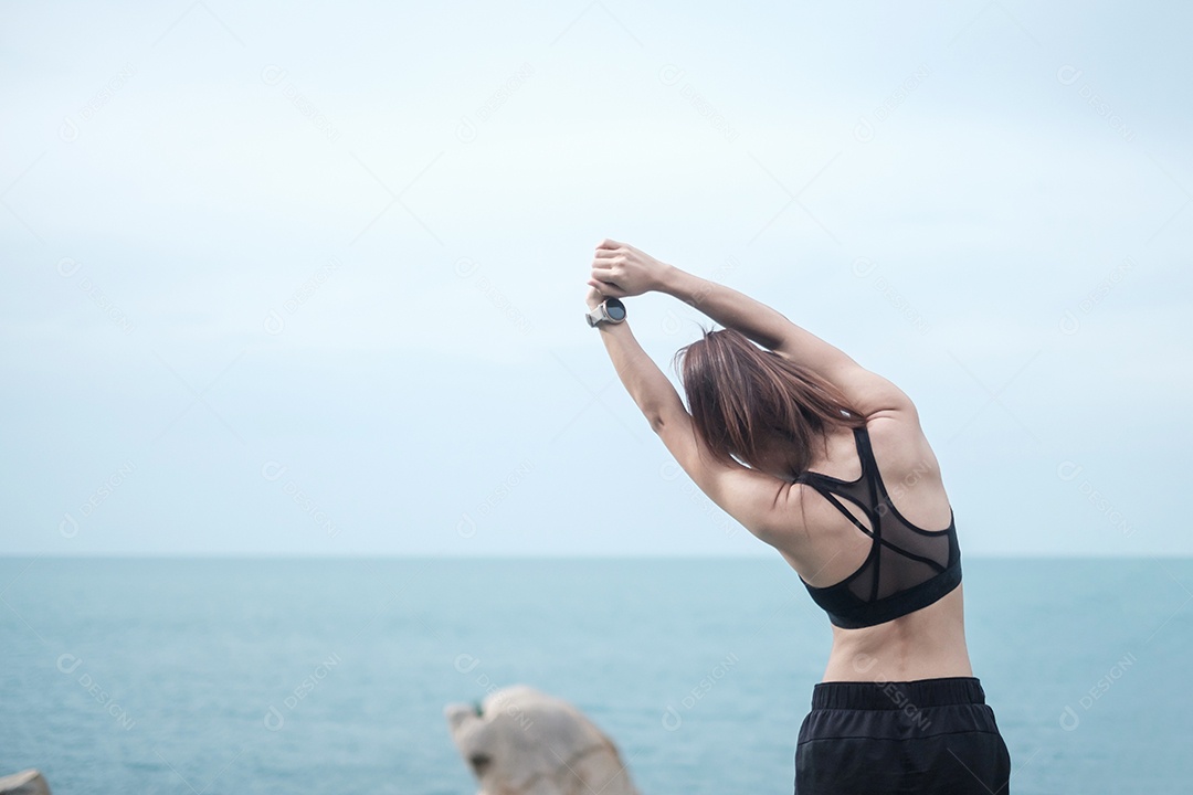 Fêmea jovem fitness em roupas esportivas esticando o corpo contra o oceano.