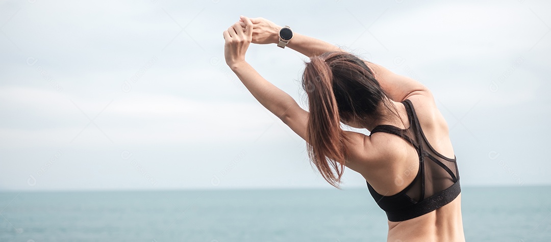 Fêmea jovem fitness em roupas esportivas esticando o corpo contra o oceano.