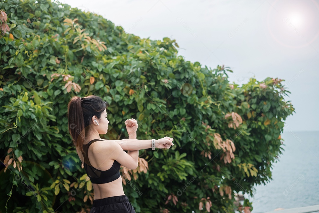 Fêmea jovem fitness em roupas esportivas esticando o corpo contra o oceano.