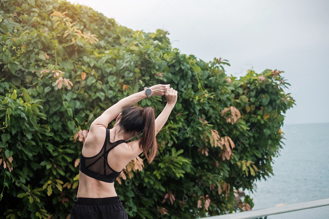 Fêmea jovem fitness em roupas esportivas esticando o corpo contra o oceano.