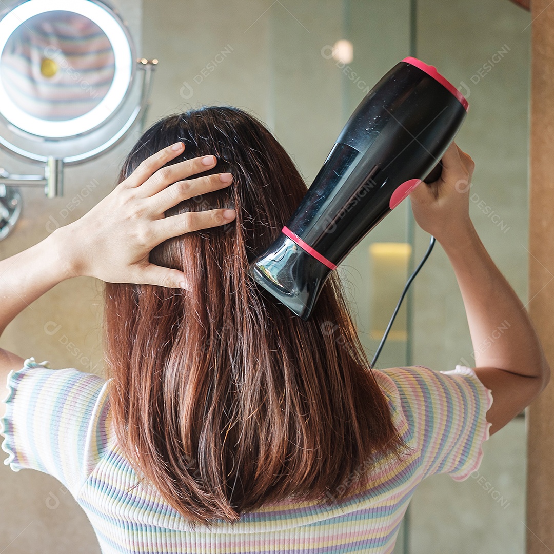 jovem mulher usando secador de cabelo perto do espelho em casa ou hotel.