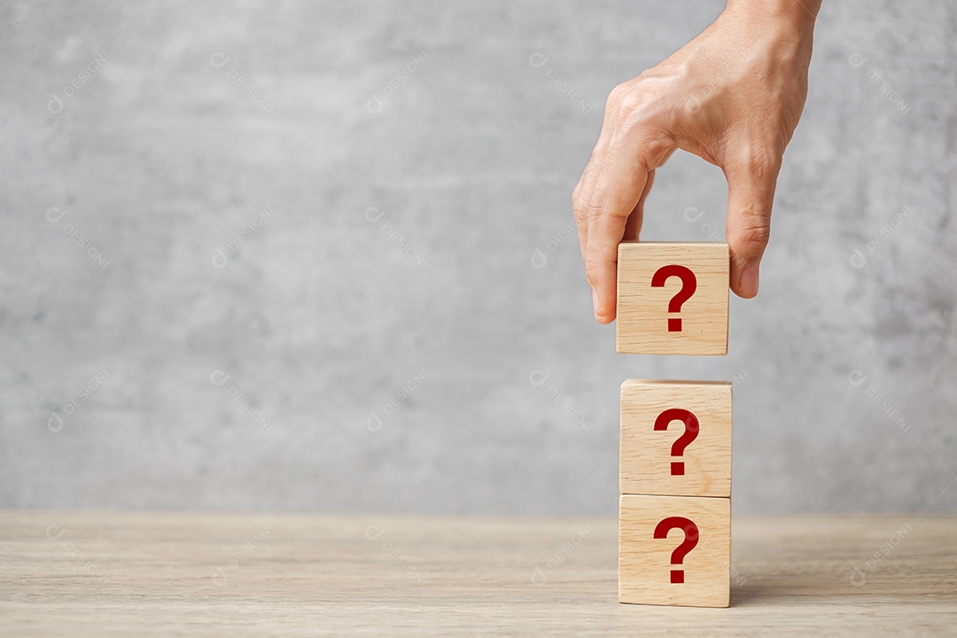 Mão segurando a marca de perguntas (?) no bloco de cubo na mesa.