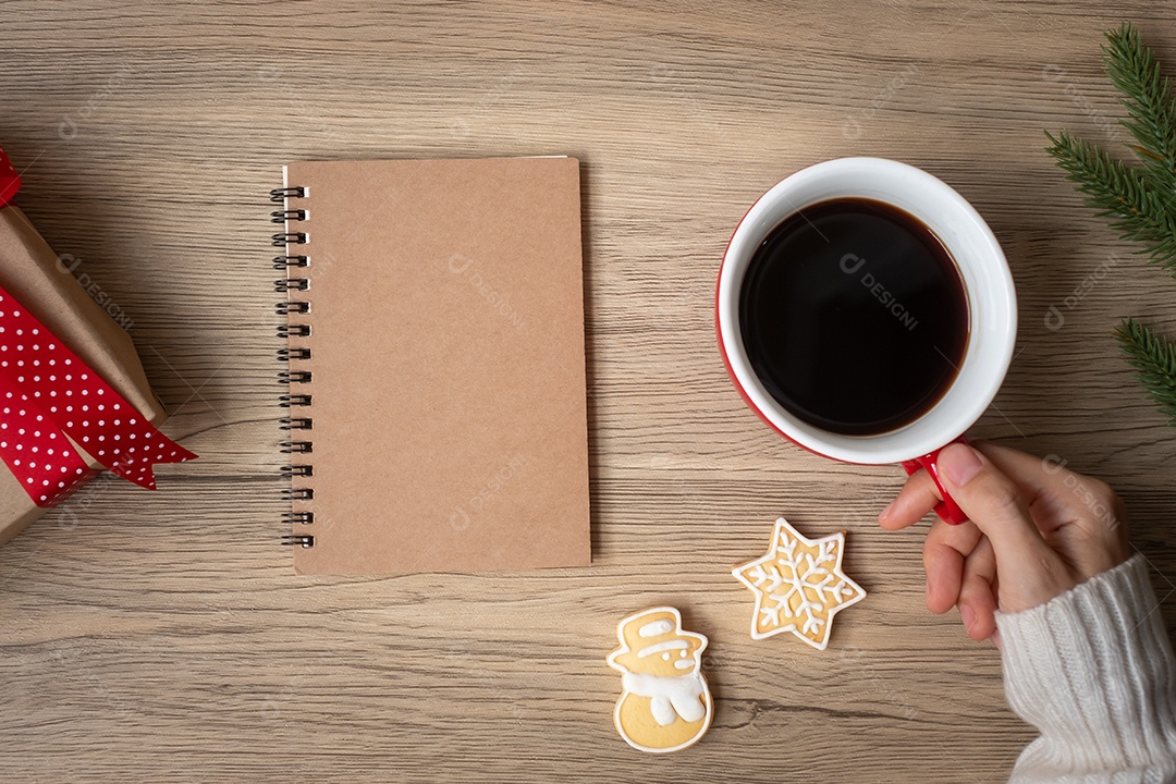 Mão de mulher segurando uma xícara de café preto com caderno em branco.