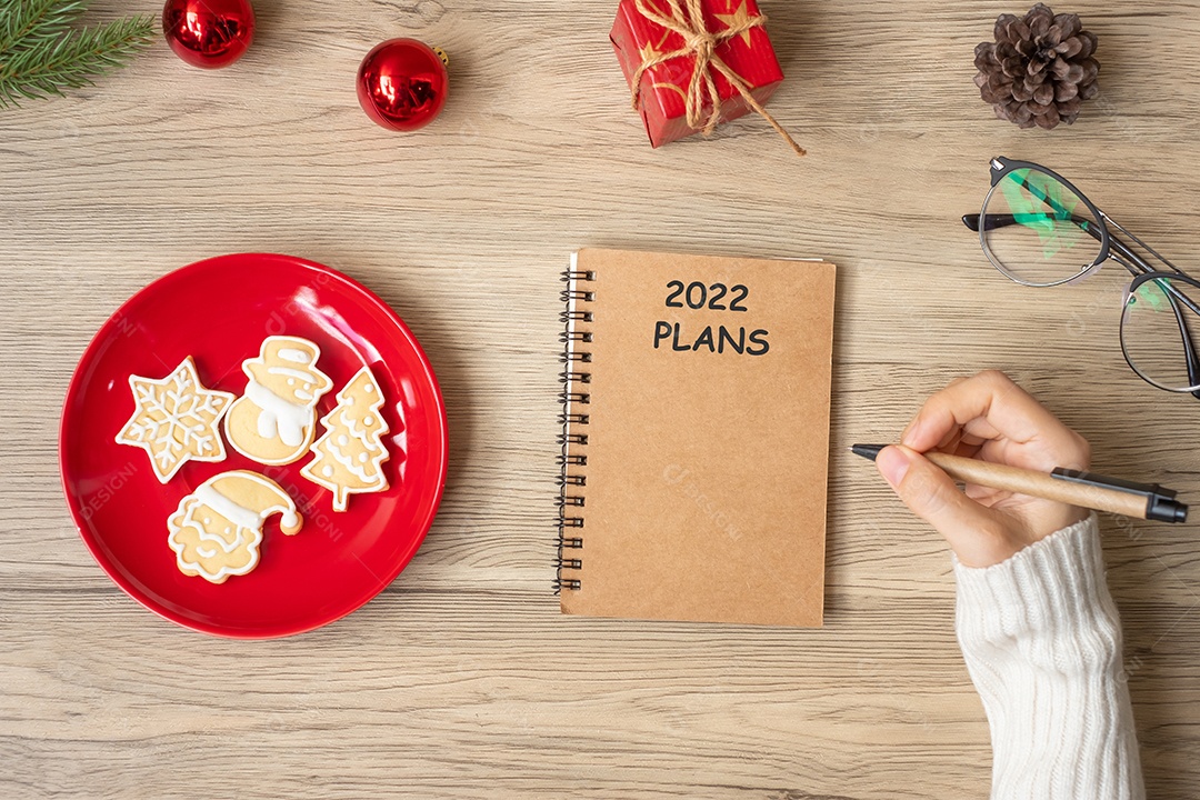 Mão de mulher escrevendo PLANOS 2022 no notebook com biscoitos de Natal.