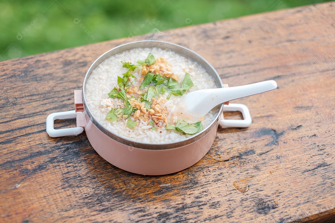 Mingau de porco ou sopa de arroz com carne de porco e legumes na mesa de madeira.