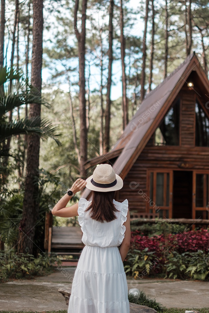 Mulher feliz de vestido branco e chapéu viajando na floresta de pinheiros.