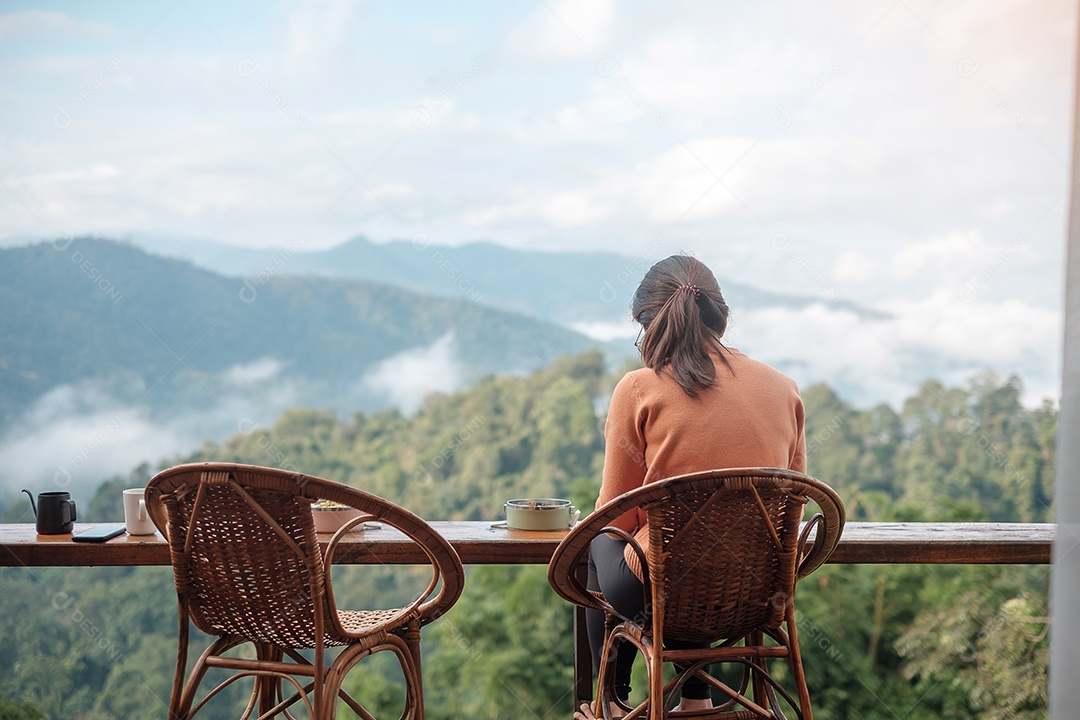 Mulher feliz tomando café e tomando café da manhã contra a montanha.