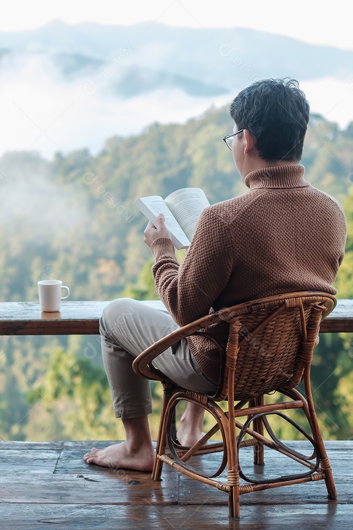 Jovem lendo livro perto da janela e olhando a vista para a montanha.