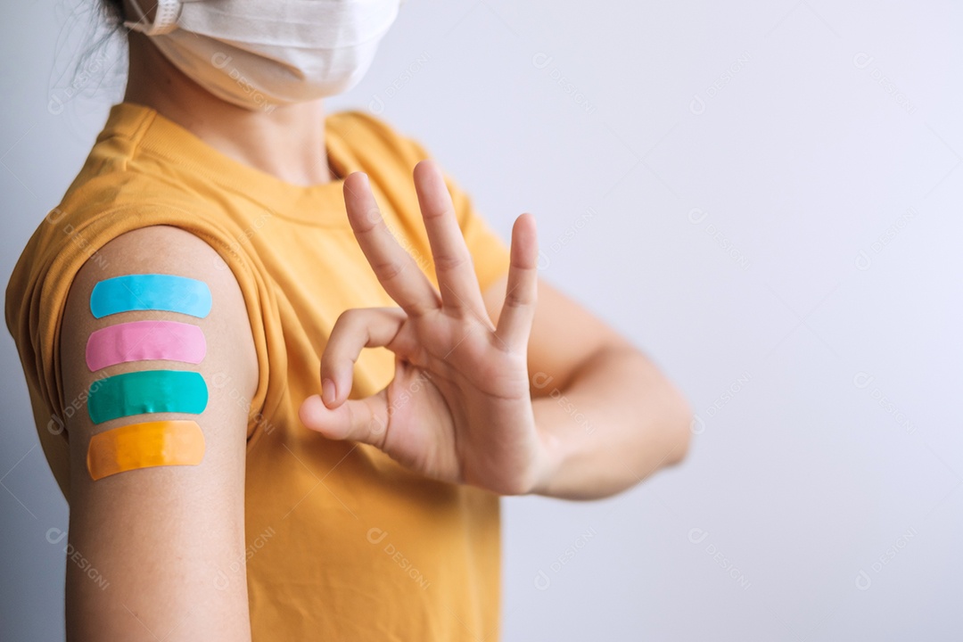 mulher mostrando sinal de polegar com curativo após receber covid 19