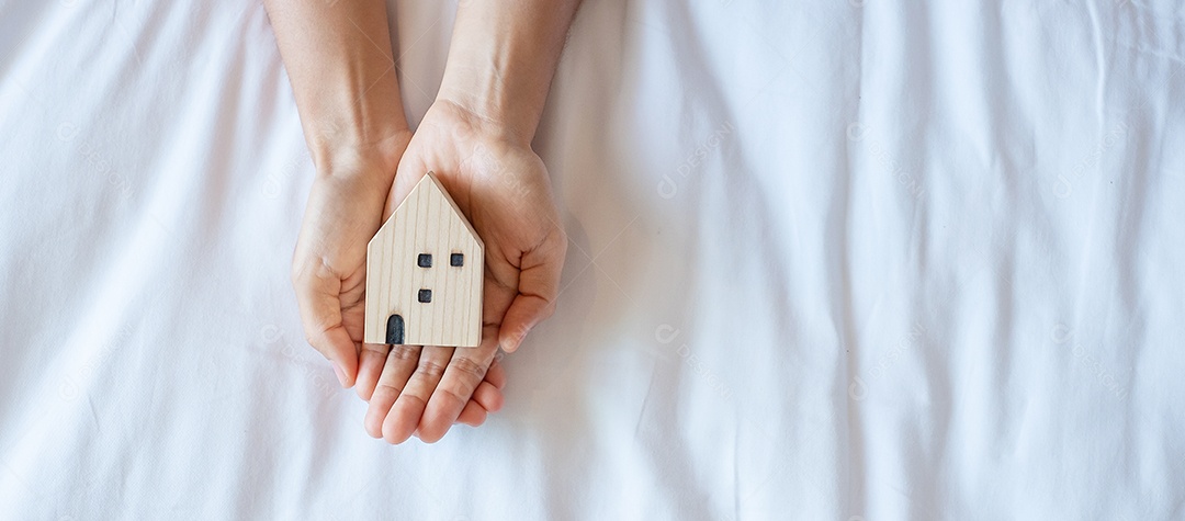 Mãos segurando um modelo de casa em fundo branco, com espaço de cópia.