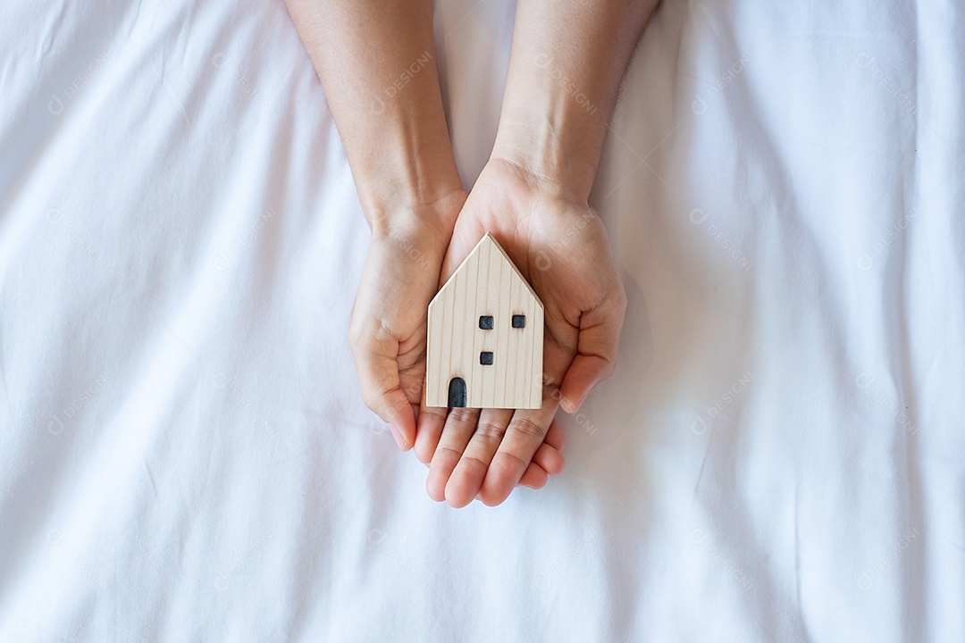 Mãos segurando um modelo de casa em fundo branco, com espaço de cópia.