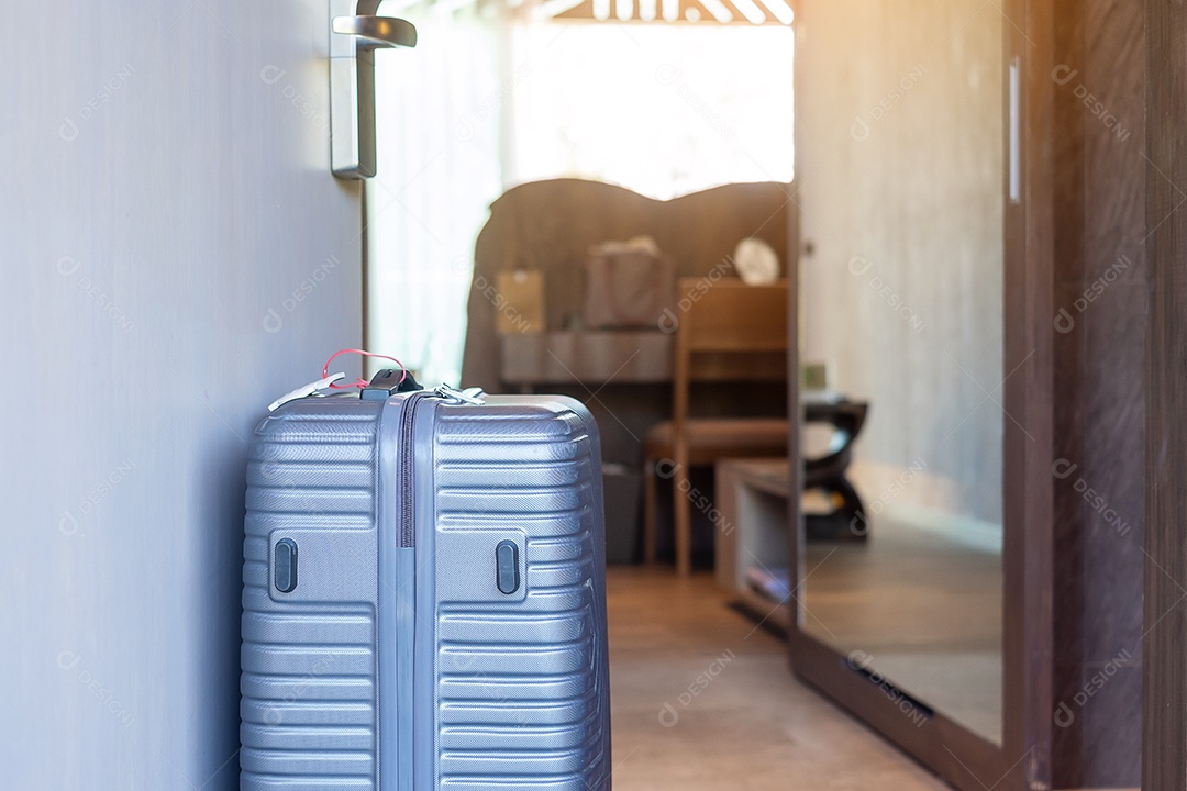 Bagagem cinzenta no quarto de hotel moderno com janelas, cortinas e cama.