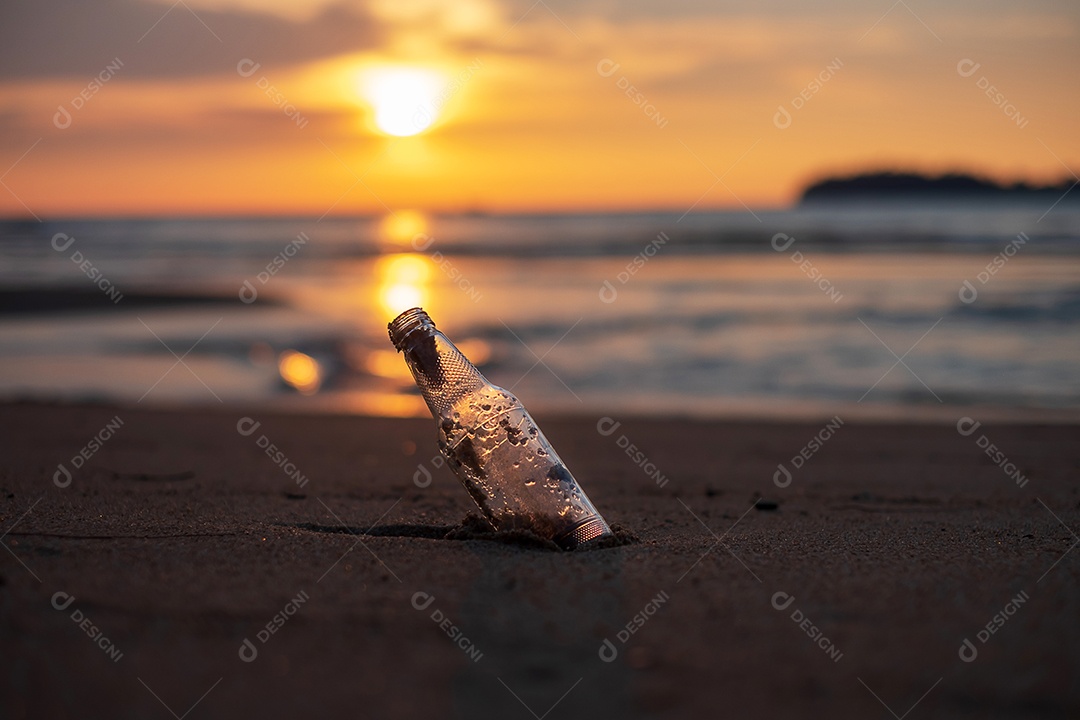 Lixo de garrafa de vidro na praia contra o fundo por do sol.