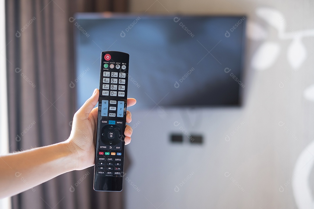 Mão usando o controle remoto para ajustar a Smart TV dentro da sala moderna em casa ou hotel de luxo