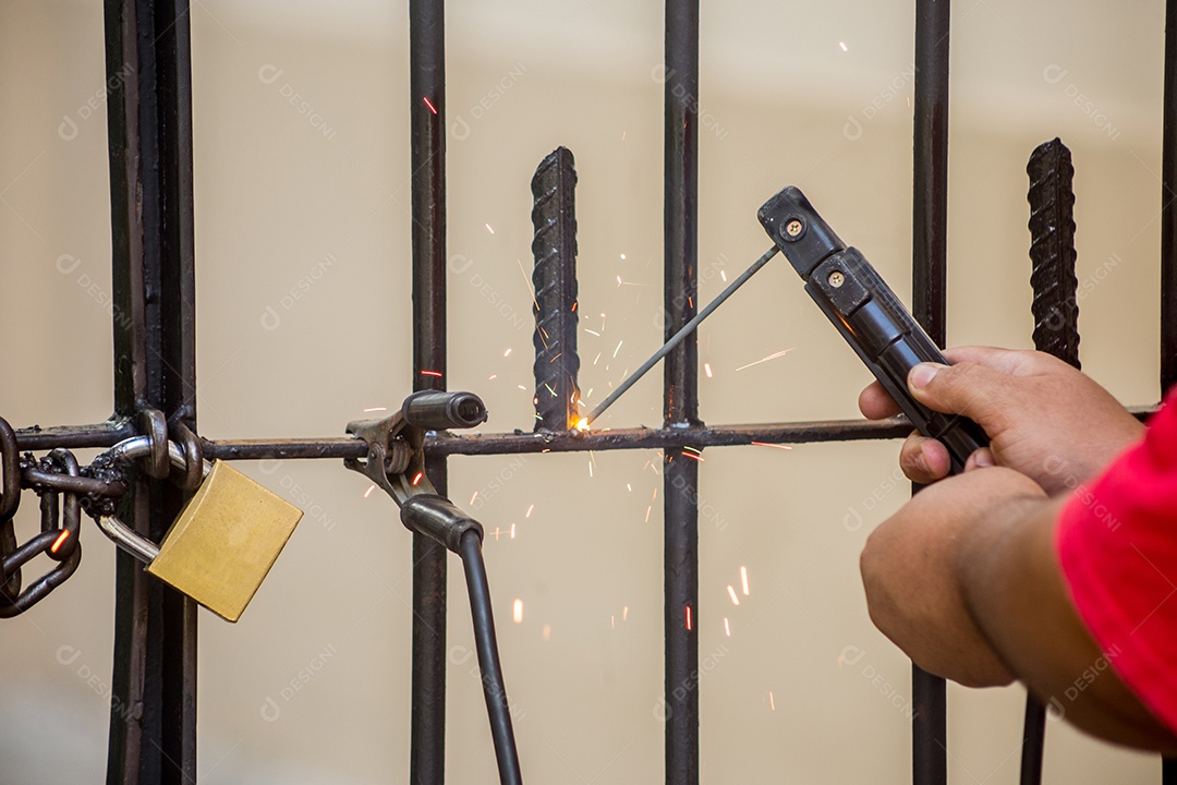 homem usando soldagem de um pedaço de ferro em um portão externo no Rio de Janeiro.