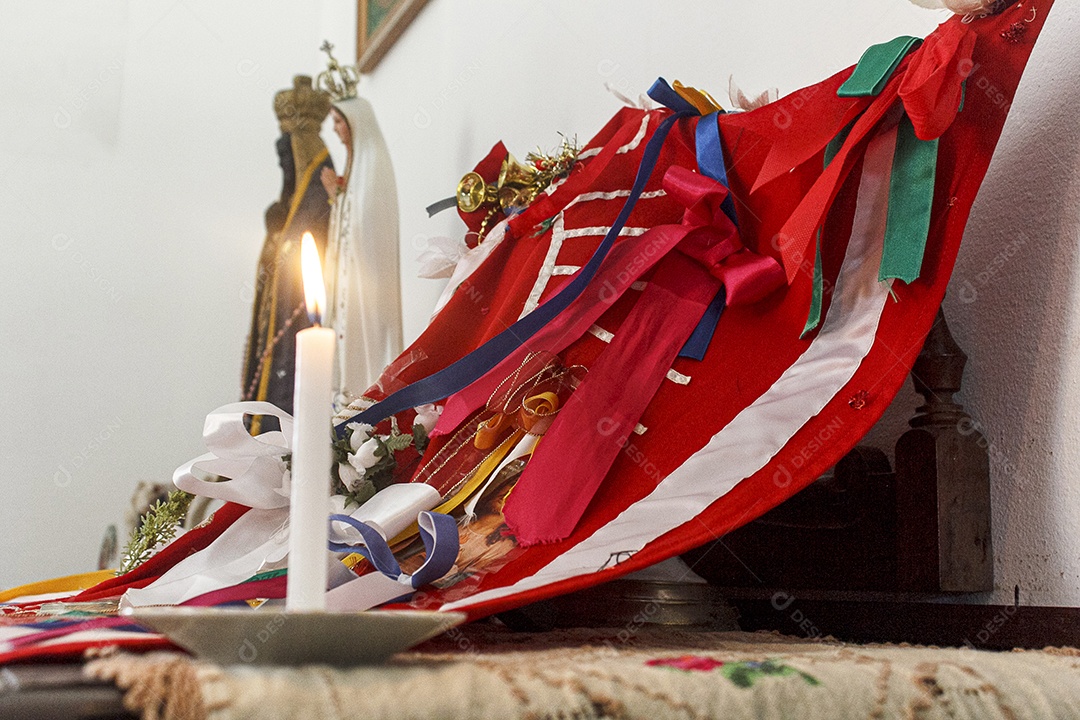 estandarte de folia de reis com vela na mesa, com as imagens de nossa senhora e nossa aparecendo ao fundo antes