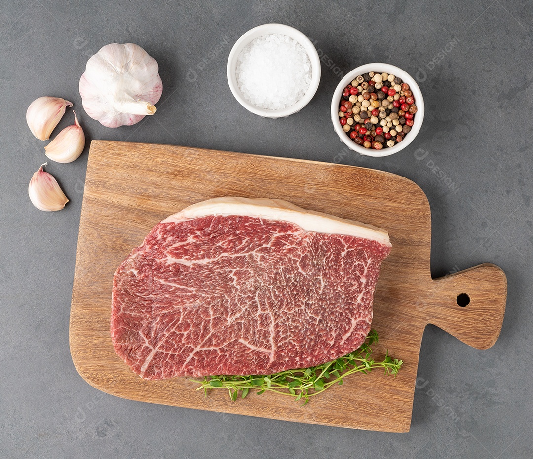 Carne assada de ombro wagyu crua sobre tábua de madeira com temperos.