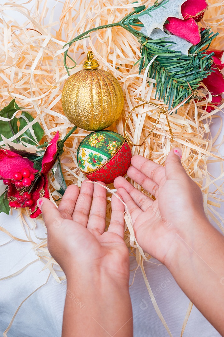 mão de criança com bolas para decoração de Natal em um fundo de palha no Rio de Janeiro.