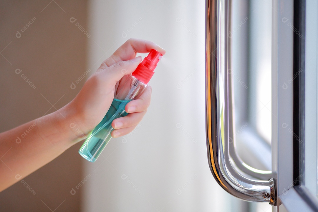 A mão da mulher está pulverizando álcool, spray desinfetante na porta do local de trabalho para segurança, prevenir a infecção do vírus Covid-19, contaminação de germes ou bactérias, limpe as superfícies que são frequentemente tocadas.