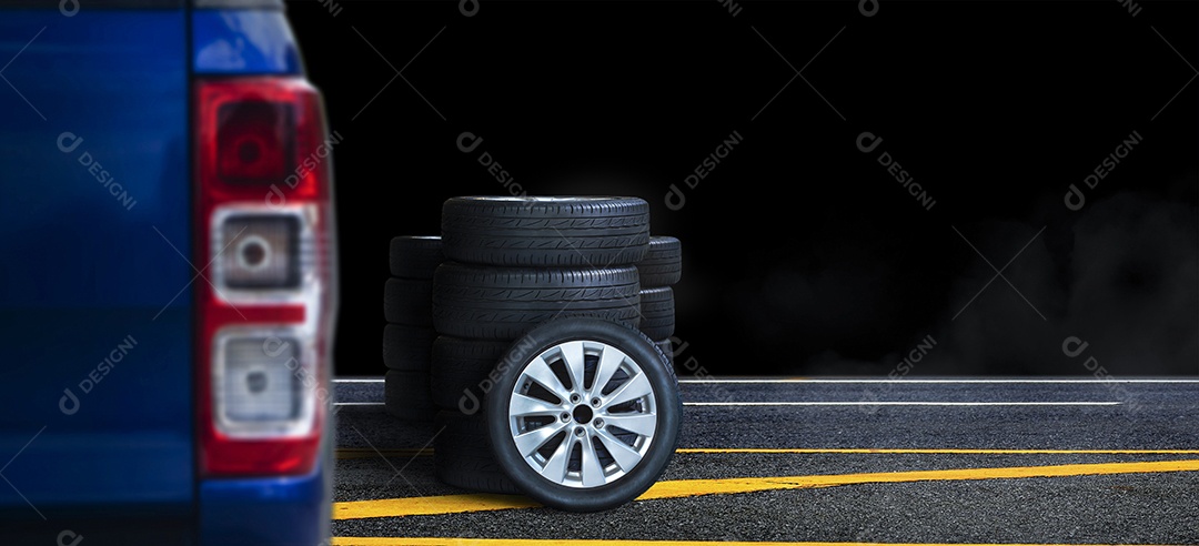 A pilha da roda e do pneu na estrada asfaltada com fundo preto