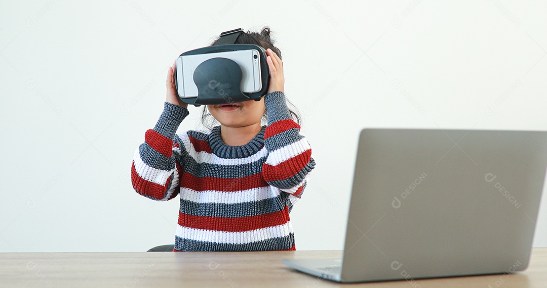 A garotinha vestindo sentada na mesa de óculos realidade virtual em casa