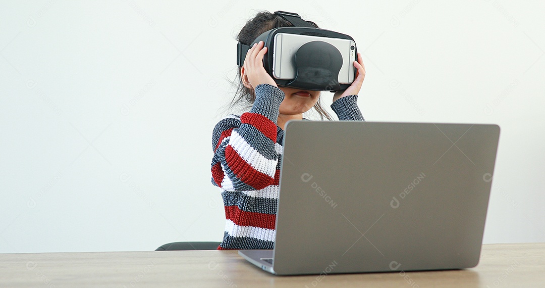 A garotinha vestindo sentada na mesa de óculos realidade virtual em casa