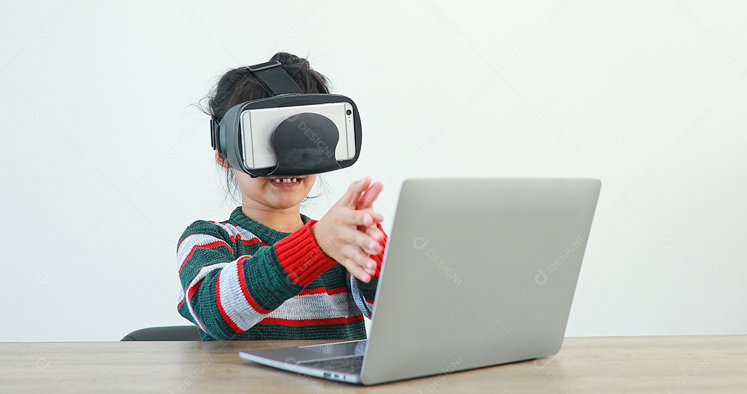 A garotinha vestindo sentada na mesa de óculos realidade virtual em casa