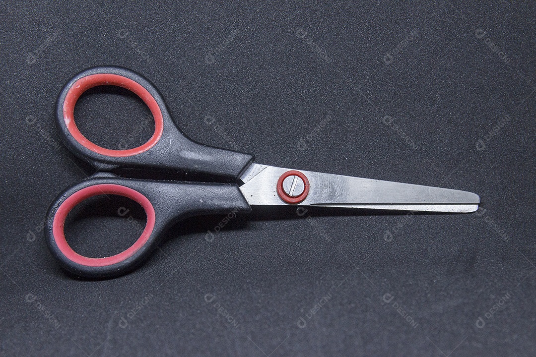tesoura com cabo preto com detalhe vermelho sobre fundo preto.