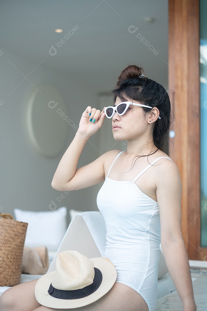 Mulher feliz em maiô branco nadando no hotel de luxo com piscina.