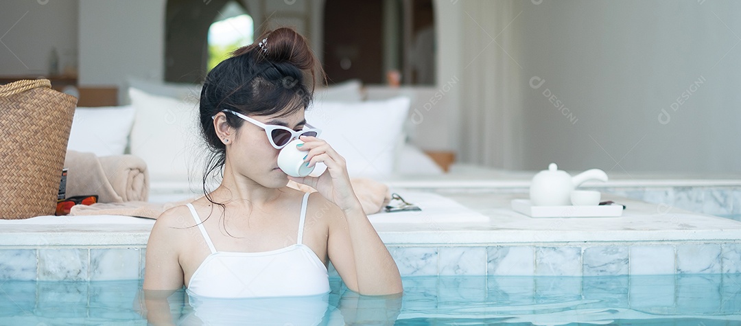 Mulher feliz em maiô branco bebendo chá quente em banho de luxo.