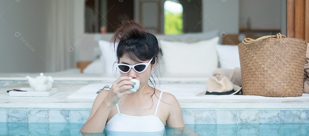 Mulher feliz em maiô branco bebendo chá quente em banho de luxo.