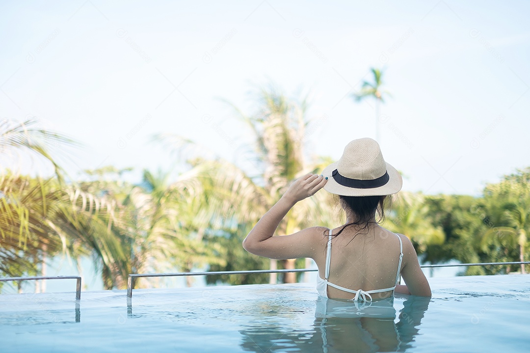 Mulher feliz em maiô branco nadando no hotel de luxo com piscina.