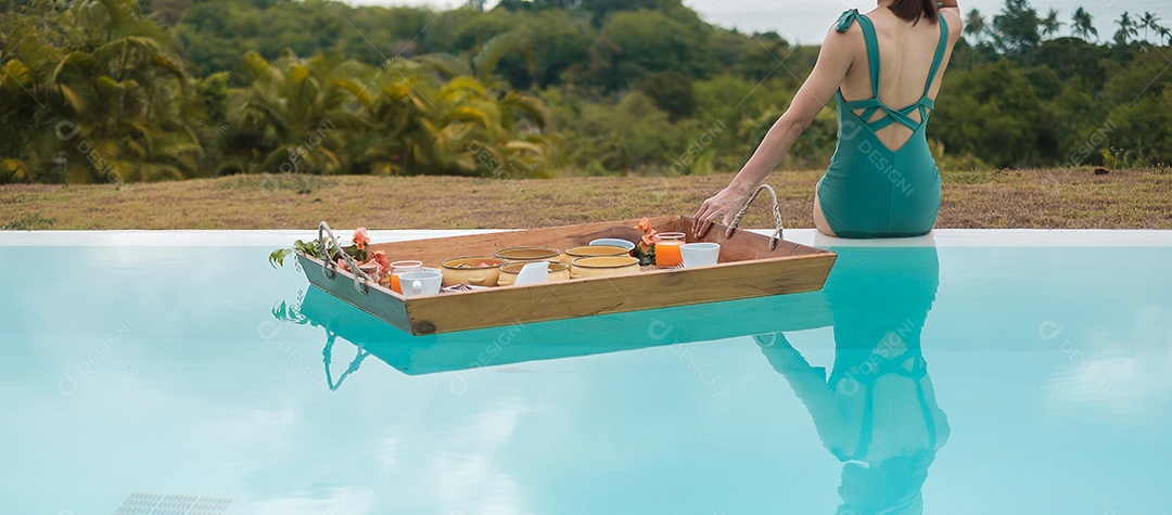 Mulher jovem feliz em traje de banho verde tomando café da manhã flutuante