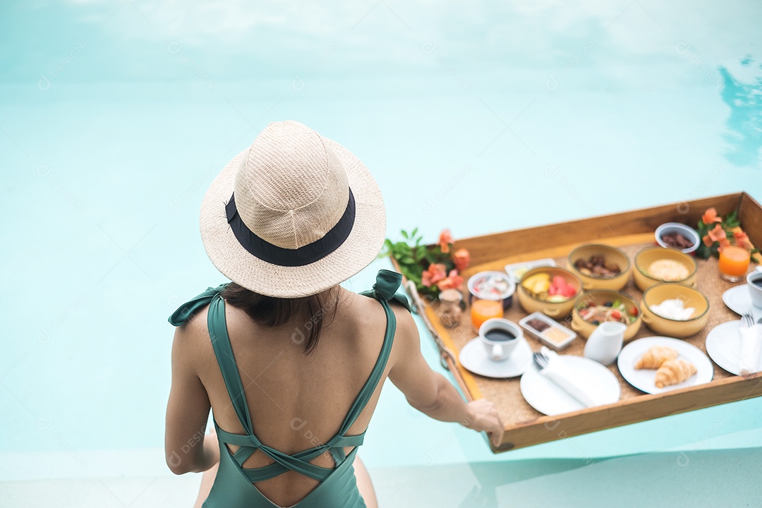 Mulher jovem feliz em traje de banho verde tomando café da manhã flutuante