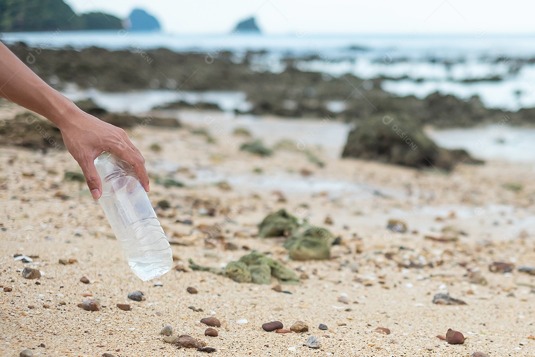 Mão voluntária pega lixo de garrafa de plástico na praia