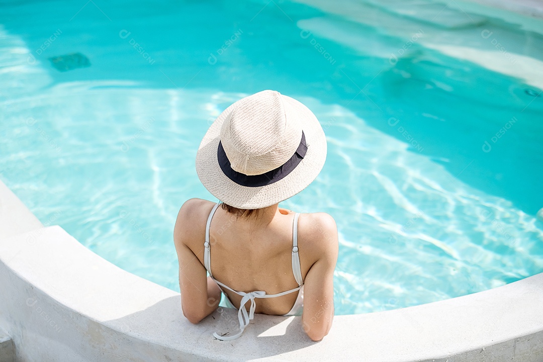 Mulher feliz em maiô branco nadando na piscina de luxo hotel