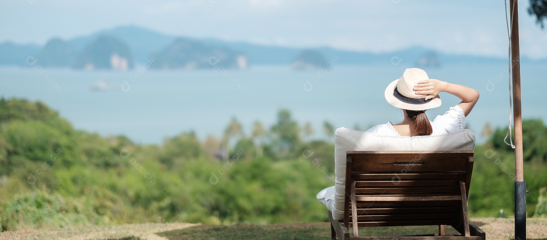 Feliz viajante de vestido branco e chapéu desfruta de uma bela vista para o mar