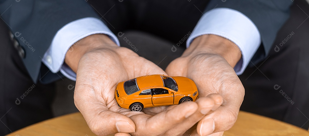 Mão de empresário segurando o brinquedo de carro laranja na mesa. Financeiro