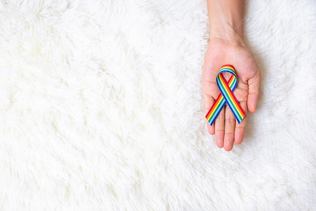 mão mostrando a fita LGBTQ Rainbow no fundo da cama branca. Suponha