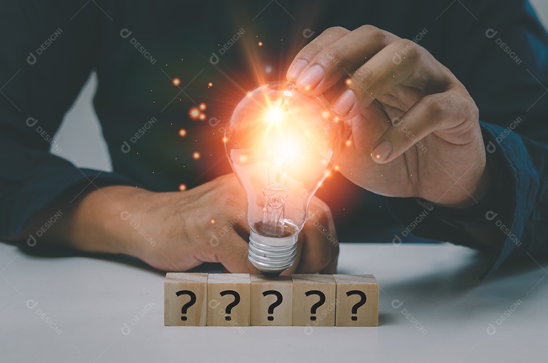 Solução de inovação de conceito de negócio de inspiração de ideia de sucesso criativo Na mesa está uma mão segurando uma lâmpada e um ícone de texto de ponto de interrogação de bloco de cubo de madeira.