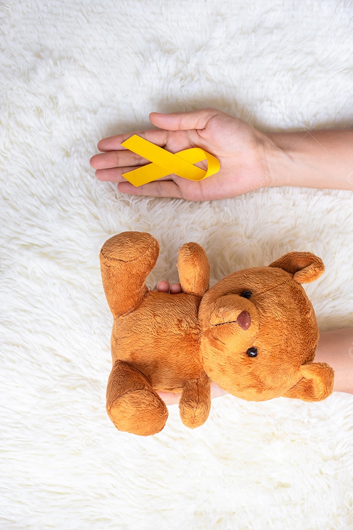 mão segurando a boneca de fita amarela e urso em fundo branco