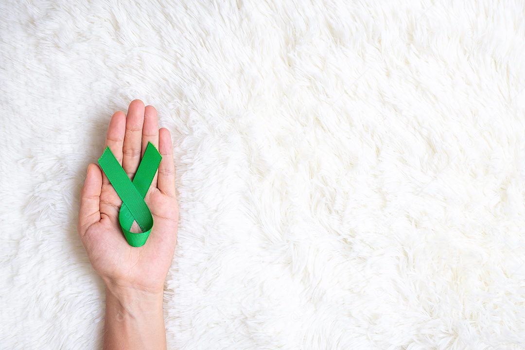 Mão segurando a fita verde para apoiar as pessoas que vivem e doentes