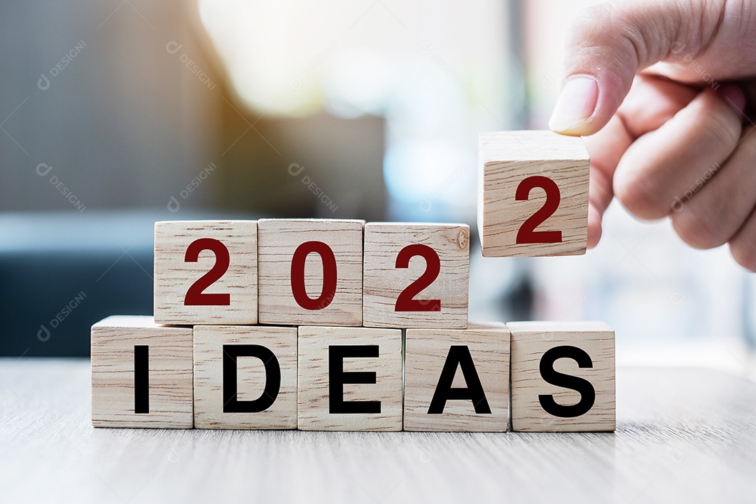 Mão de empresário segurando o cubo de madeira com flip over block 2022 IDEAS word no fundo da mesa. Resolução, estratégia, solução, objetivo, negócios e conceitos de feriado de ano novo