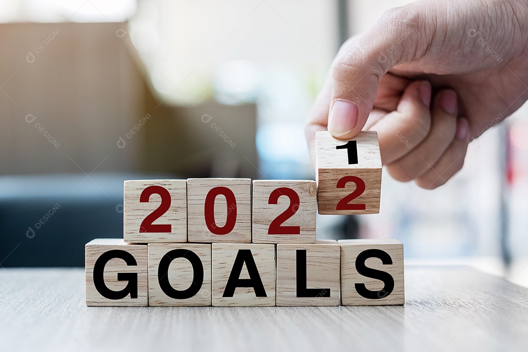 Mão de empresário segurando cubo de madeira com flip over block 2021 a 2022 GOALS word no fundo da mesa. Resolução, estratégia, solução, objetivo, negócios e conceitos de feriado de ano novo